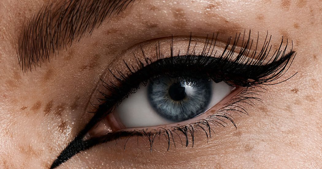 blaues Auge mit schwarzem Eyeliner, langen Wimpern und Sommersprossen