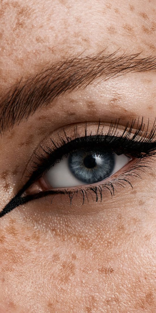 blaues Auge mit schwarzem Eyeliner, langen Wimpern und Sommersprossen